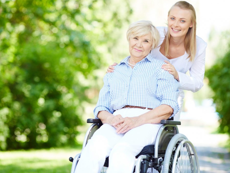 Female caregiver and senior patient in a wheelchair looking at camera outside